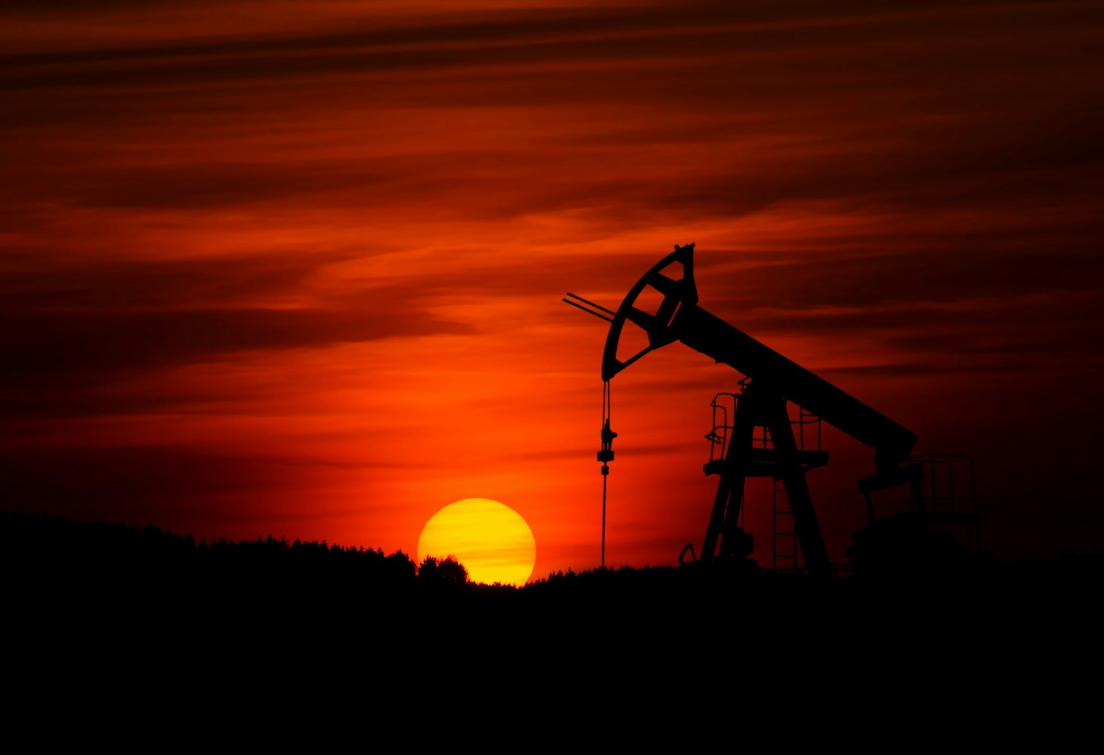 Un balancín petrolero recortado contra una puesta de sol roja.