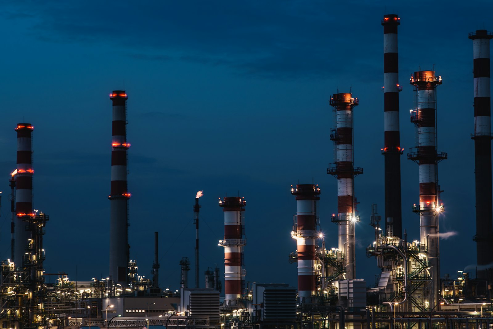 Torres de una refinería de petróleo iluminadas contra un cielo del atardecer.